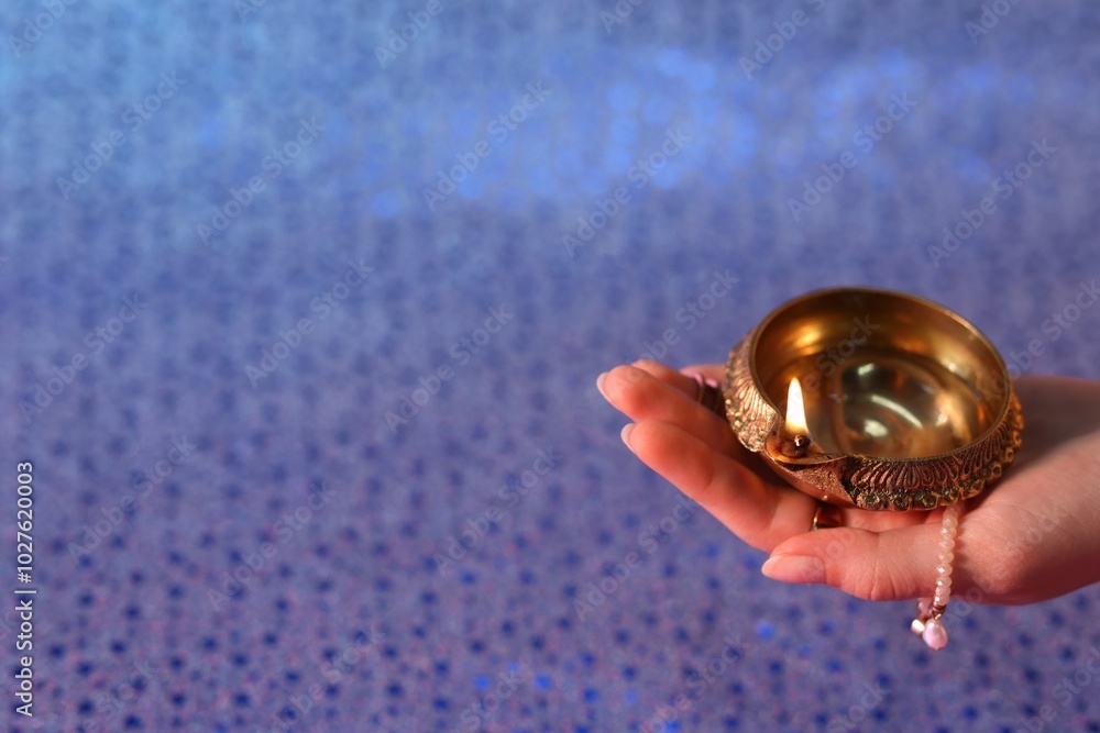 Canvas Prints Diwali celebration. Woman holding lit diya lamp on color background, closeup. Space for text