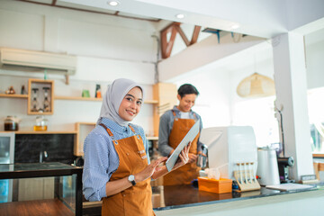 veiled female waitress using a tablet against the background of male waiters in a coffee shop