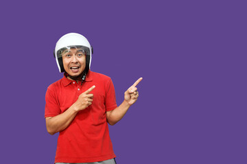 Young Asian driver man wearing helmet looking up while raising both hands and pointing upwards with happy expression
