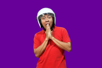Mature Asian man wearing a motorbike helmet with a surprised face on a purple background With copy space
