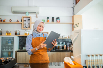 Woman in hijab cafe owner wearing apron using a tablet at coffee cafe