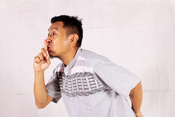 Asian man giving silent sign by touching his mouth on white background

