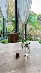 The vase is placed on a wooden table with a view of the trees outside.