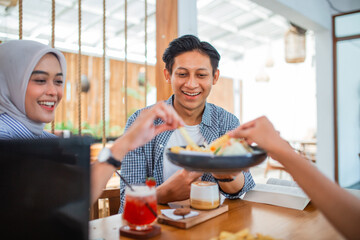 young Asian man smiling while enjoying a snack with friends at a coffee shop