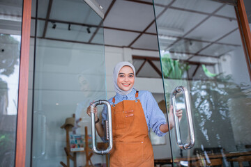 veiled woman wearing an apron opens the front door of a coffee shop
