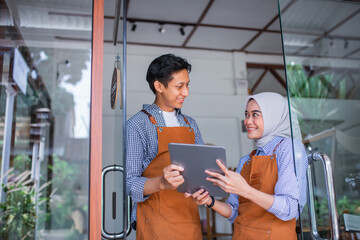 veiled woman and male waiter using a tablet together standing in front of a coffee shop