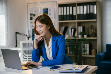Obraz premium Young professional woman works happily at a modern office desk, surrounded by paperwork and technology, showcasing her corporate and entrepreneurial skills