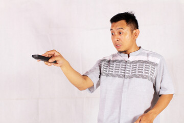 Asian man holding tv remote with surprised and confused expression
