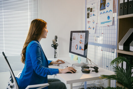 Businesswoman is working at her desk, analyzing financial data displayed on her computer screen.  She is smiling as she prepares for an upcoming presentation