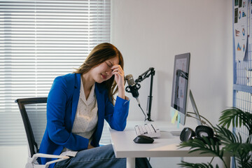 Businesswoman is sitting at her desk with her hand on her head, experiencing a headache. She is...