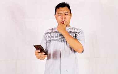 Adult Asian man showing sad and thinking feelings while looking at his cell phone