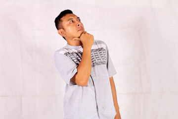 Mature Asian man thinking with pensive expression wearing blue shirt with hand on chin
