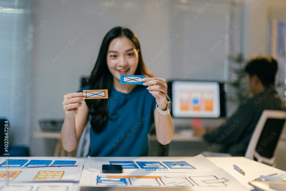 Poster young asian designer woman is holding two different options for a mobile app interface, comparing th