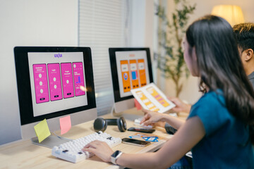 Two designers are working on a new mobile application in an office environment, comparing paper...