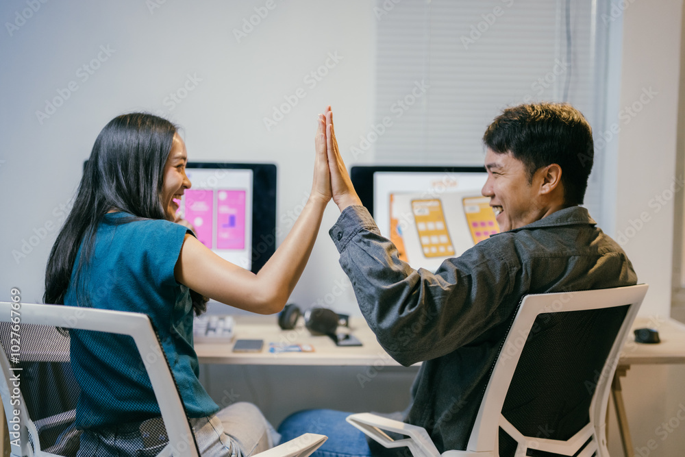 Poster Two cheerful ui/ux designers are giving high five while working at the office desk, celebrating the success of their new mobile application interface