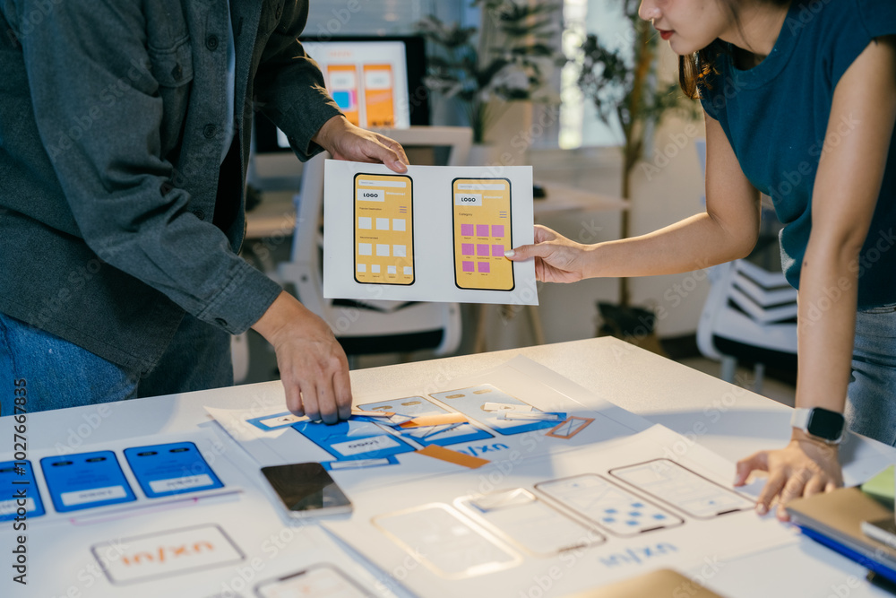 Aufkleber Web designers are reviewing the layouts of a mobile application they are developing for a client, using printed paper wireframes