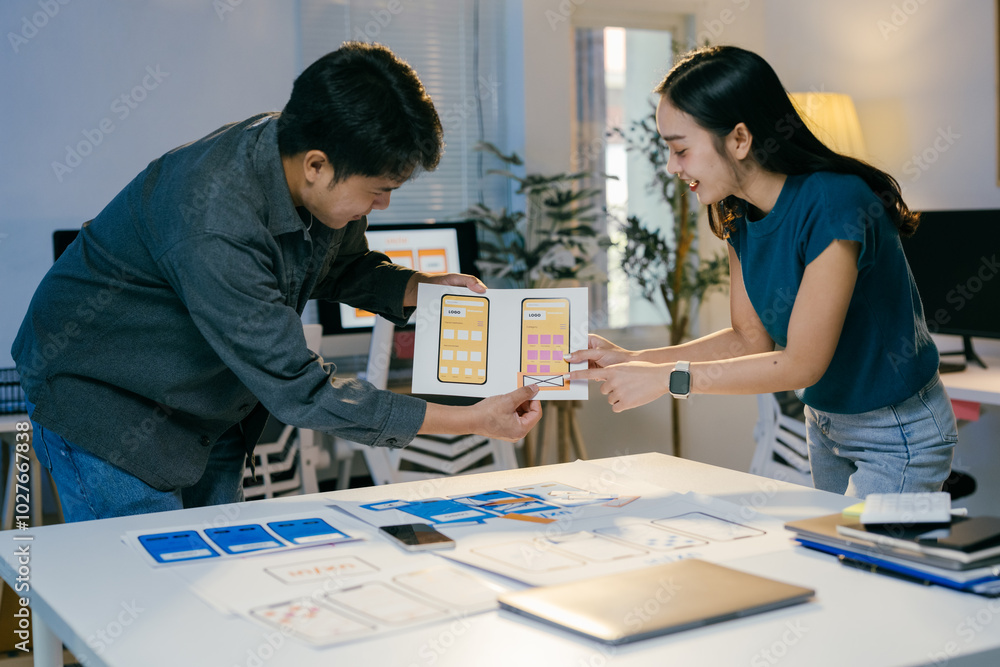 Poster Two ui designers are discussing over a mobile app interface design during a working session. They are reviewing the layout and functionality of the app