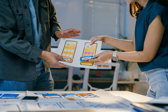 Two designers are discussing about a mobile app interface design, reviewing some paper prototypes and making some improvements