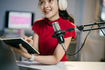 Young asian woman records a podcast in her home studio, surrounded by technology, smiling confidently as she creates digital content for her online audience