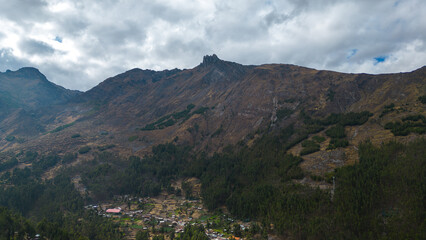 Obraz premium small rural andean village surrounded by a forest in south america with a large mountain with a pointed peak behind it on a cloudy winter day.