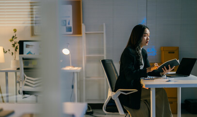 Focused businesswoman works late at night in her office, analyzing data on her laptop with determination and ambition