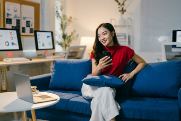 Obraz premium Young businesswoman is taking a break from work, sitting on a comfortable couch in her office and checking her smartphone