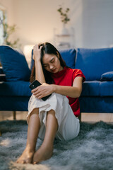 Obraz premium Sad young woman sits on the floor in her living room, clutching her phone, overwhelmed by depression and stress in today's digital age