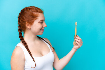 Obraz premium Young caucasian reddish woman brushing teeth isolated on blue background with happy expression