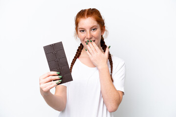 Young reddish woman isolated on white background taking a chocolate tablet and surprised