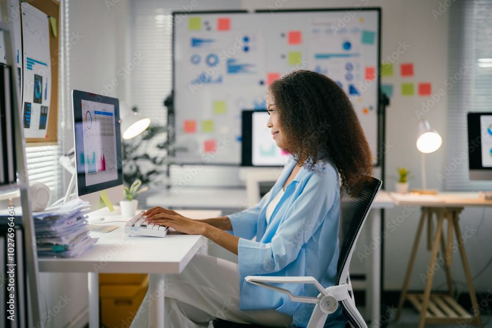 Poster young professional is analyzing data on her computer in a bright, modern office. she is surrounded b