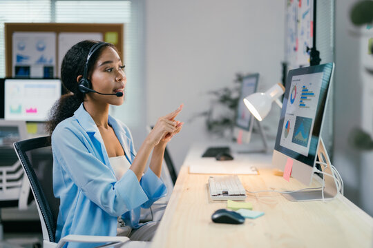 African american businesswoman wearing a headset is speaking and gesturing while participating in a video conference on her computer - Powered by Adobe