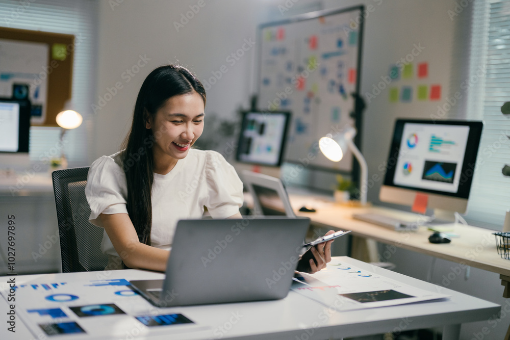 Poster young professional is analyzing charts and graphs on her laptop while holding a digital tablet in he