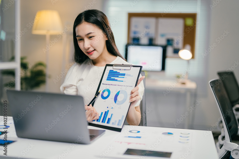 Poster businesswoman is presenting charts and graphs on a video call from her brightly lit office at night.