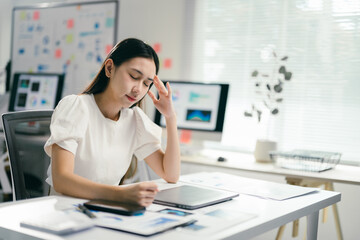 Young businesswoman is feeling tired and having a headache while working in the office. She is touching her head with her hand, showing her exhaustion