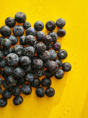 Fresh blueberries on a bright yellow background, with water droplets enhancing their freshness.