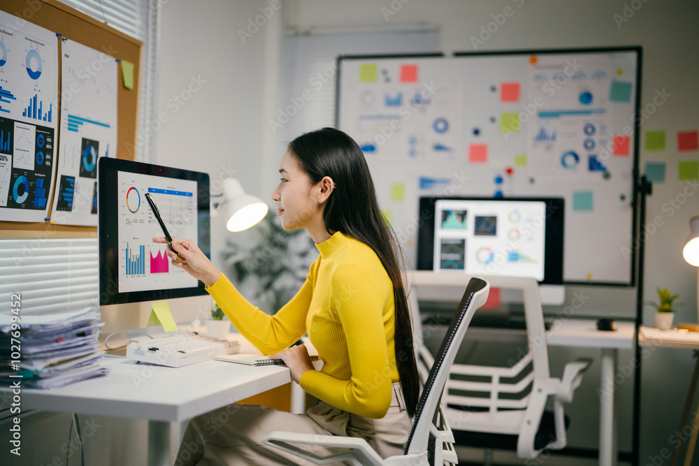 Aufkleber Young professional is reviewing data on her computer, surrounded by charts and graphs in a bright and modern office setting