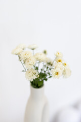 A simple vase of white flowers on a minimalist table against a soft, neutral backdrop in a serene indoor setting