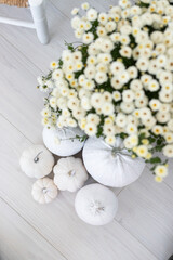 A cozy autumn arrangement featuring white pumpkins and delicate white flowers on a wooden floor in a softly lit room