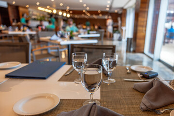 Elegant restaurant table set with glasses with water and plates, with soft lighting and people dining in blurred background. Mexico.