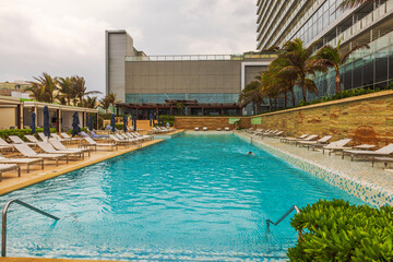 Luxurious hotel outdoor pool with lounge chairs and modern architecture in background, surrounded by tropical plants and palm trees. Mexico.