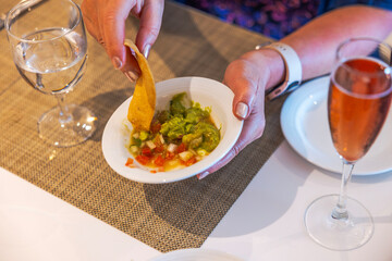 Close-up view of person dipping chip into guacamole with glass of  wine and water on table. Mexico.