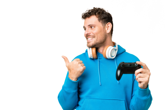 Brazilian man playing with a video game controller over isolated chroma key background pointing to the side to present a product - Powered by Adobe