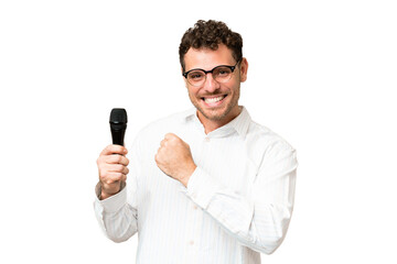 Brazilian man picking up a microphone over isolated chroma key background celebrating a victory