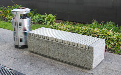 A concrete bench is next to a shiny stainless steel trash can