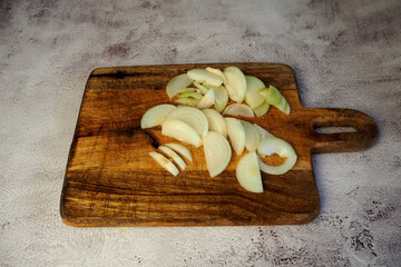 On the gray marble table lies a wooden dark brown board with two onions cut into half rings. side view kitchen. copy space