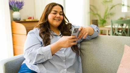 Smiling young woman relaxes on the sofa at home while using her smartphone