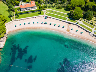 Aerial drone view of Sveti Stefan Island- Luxury travel destination in Montenegro. Waves splashing the rocks. At right is Sveti Stefan Beach. Panoramic view. Emerald water.