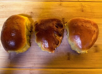 Three golden-brown Ukrainian pyrizhky (filled buns) rest on a wooden cutting board, each with a shiny, perfectly baked crust. These traditional pastries are a beloved part of Ukrainian cuisine.