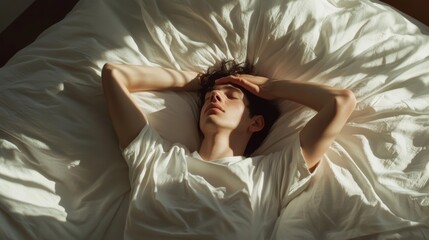 Fototapeta premium Young man is lying on his back in bed with his eyes closed, holding his head with his hands, suffering from headache or depression