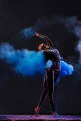 girl dancer in black suit dancing with explosions of colored paints holi on dark background